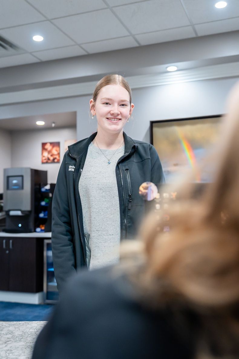 A patient smiles while standing in a brightly lit office lounge with a coffee machine and artwork in the background.