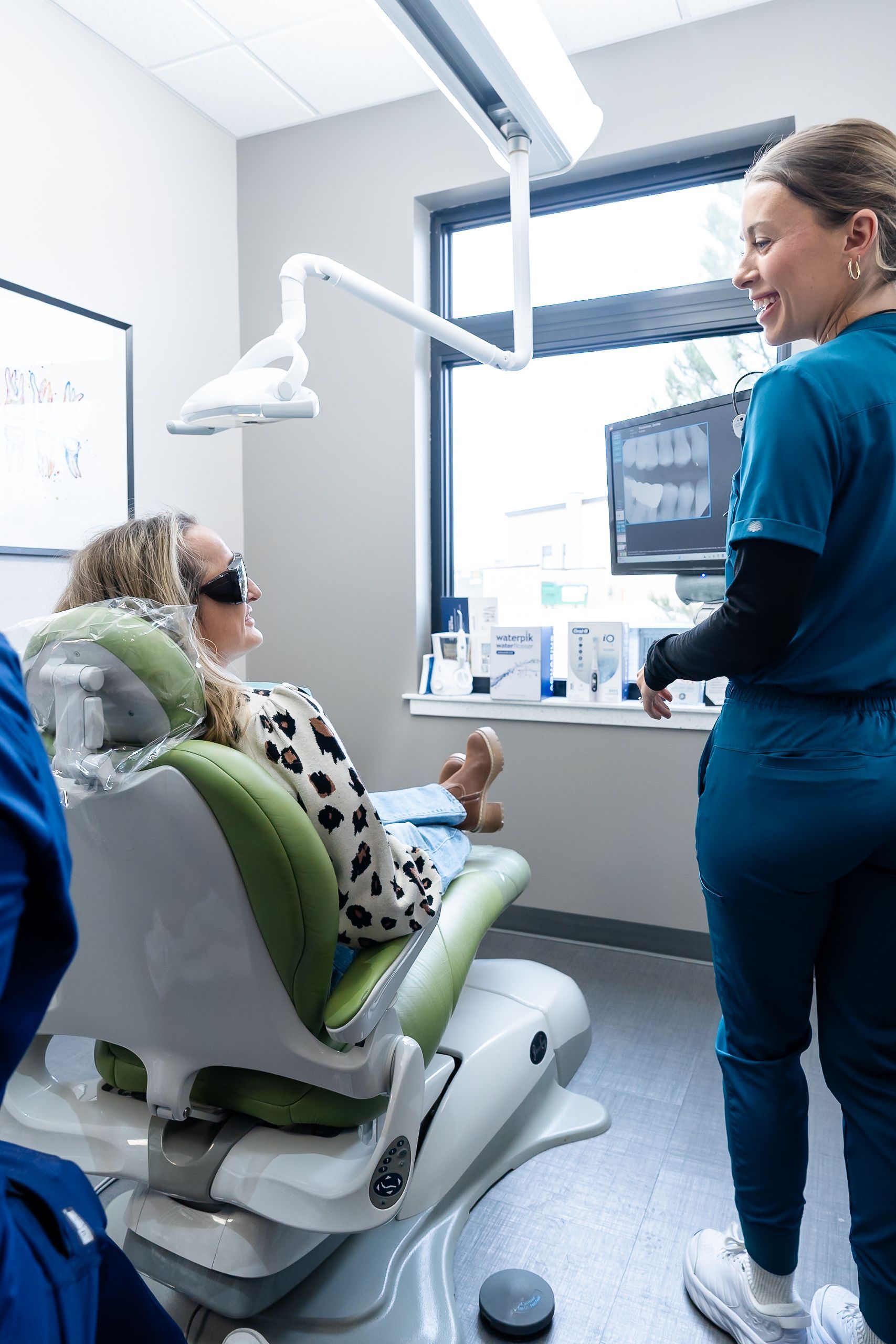 Patient in a dental chair talking with a dentist in a bright clinic room.
