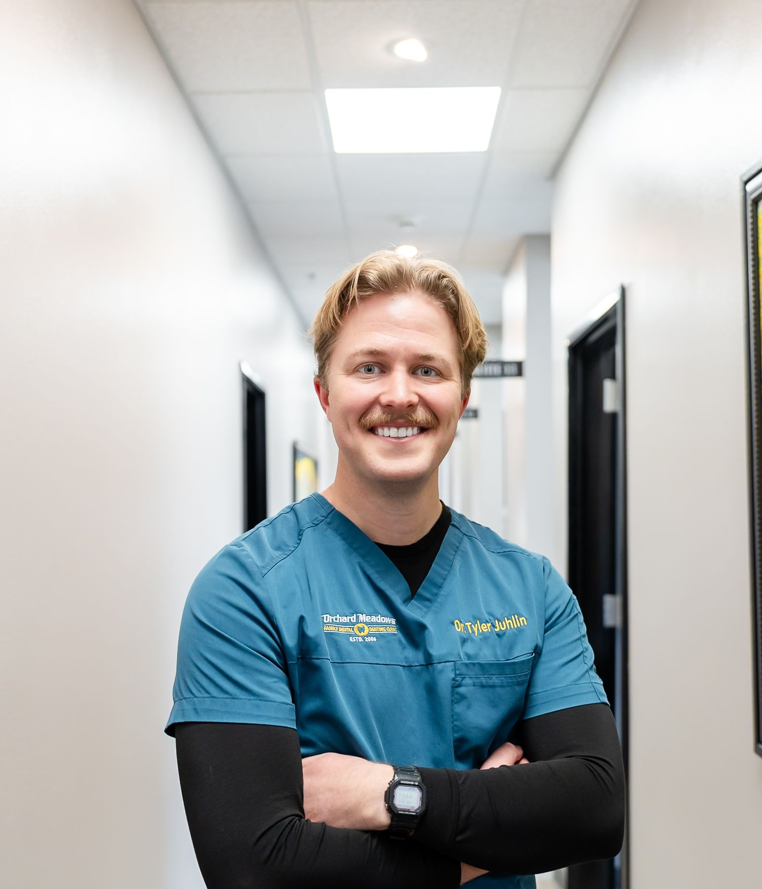 Dr. Tyler in teal scrubs and a black long-sleeved shirt standing in a hallway with arms crossed and smiling.