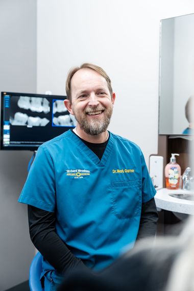 Dr. Garner sitting in a clinical exam room with dental X-rays displayed on a monitor.