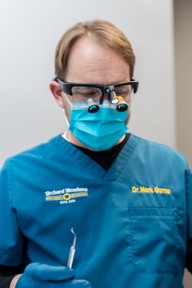 Dr. Garner in teal scrubs and a face mask wearing magnifying loupes, holding a dental tool.