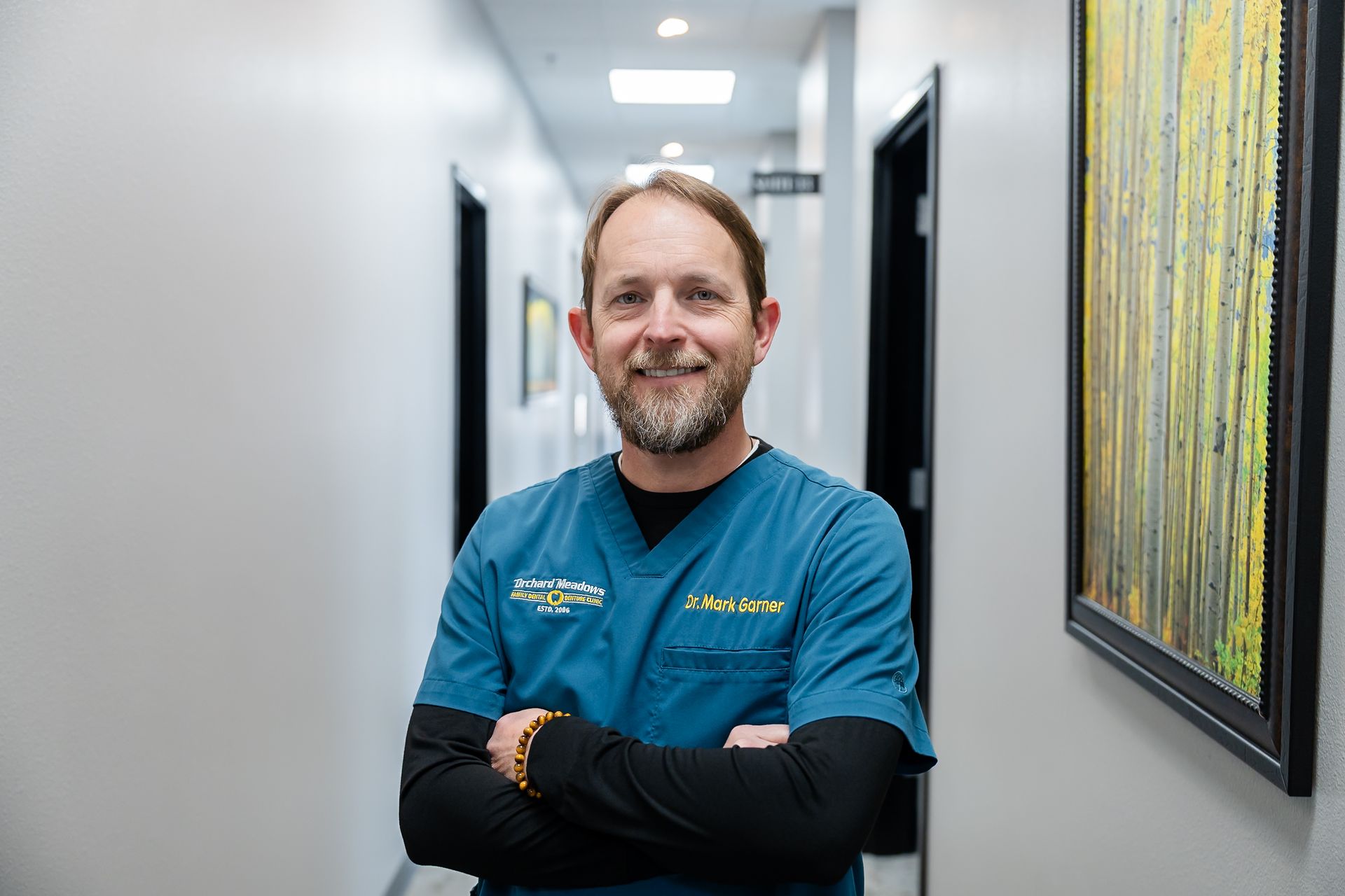 Picture of DR. Garner wearing a teal scrubs over a long-sleeved black shirt, stands with arms crossed in a hallway.