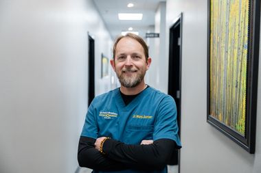 Picture of DR. Garner wearing a teal scrubs over a long-sleeved black shirt, stands with arms crossed in a hallway.