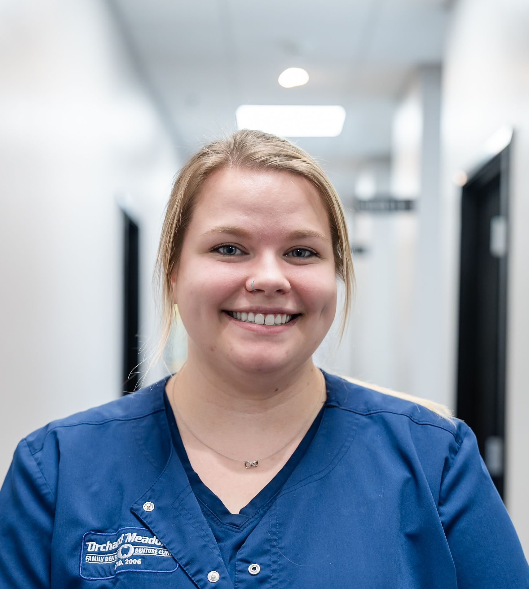 Picture of DR. Garner wearing a teal scrubs over a long-sleeved black shirt, stands with arms crossed in a hallway.