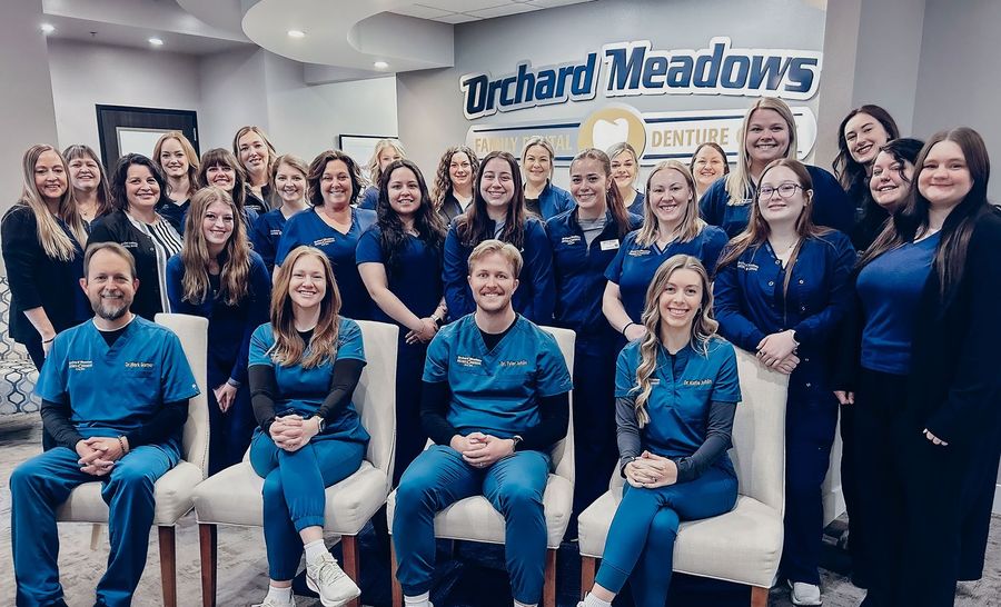 Orchard Meadows dental staff in scrubs and professional attire posing for a photo in a modern office lobby.