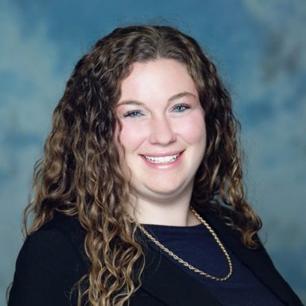 Picture of DR. Garner wearing a teal scrubs over a long-sleeved black shirt, stands with arms crossed in a hallway.