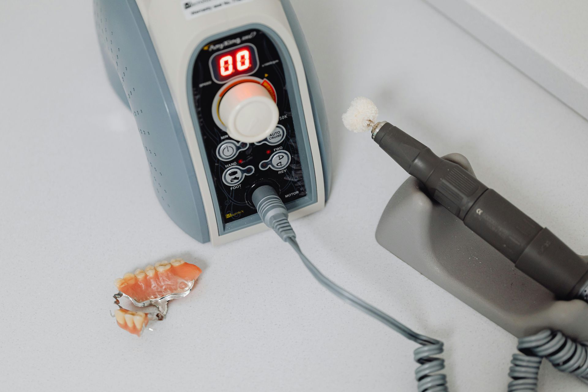 Nail drill control box with handpiece and a small shell on a white tabletop
