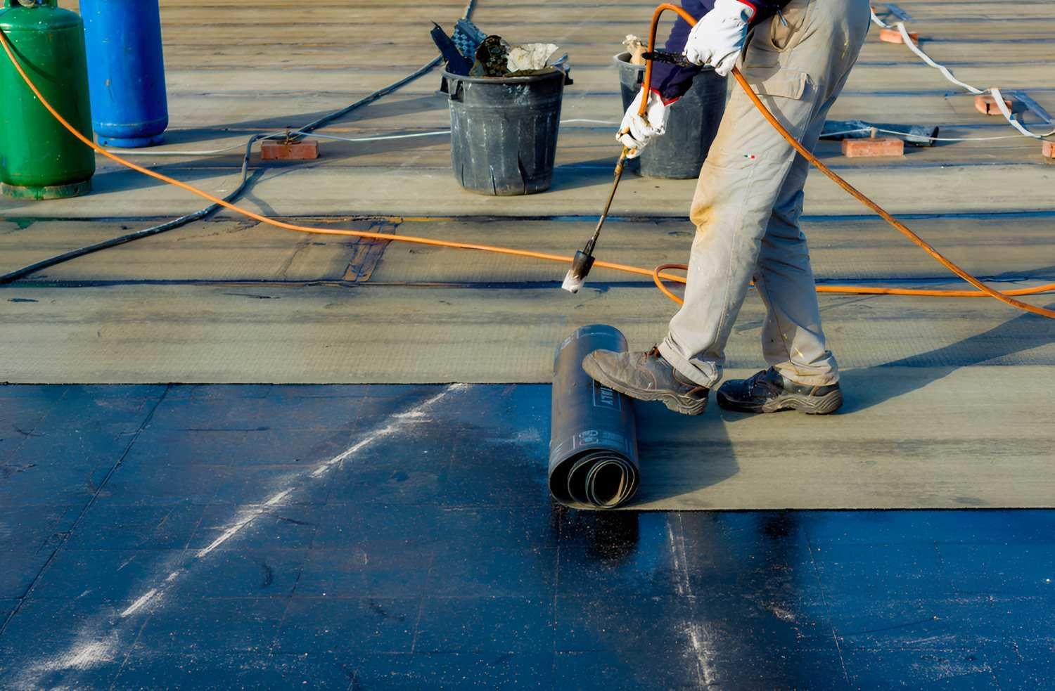 A Man Is Rolling A Roll Of Waterproofing On A Roof — Bananacoast Waterproofing in Korora, NSW