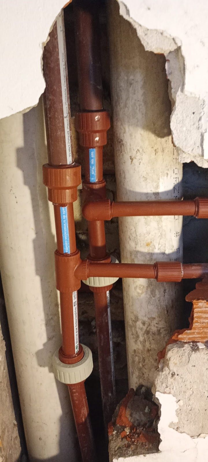 Dos técnicos con uniformes azules y grises inspeccionan una tubería de gas en la pared con herramientas en una habitación luminosa.