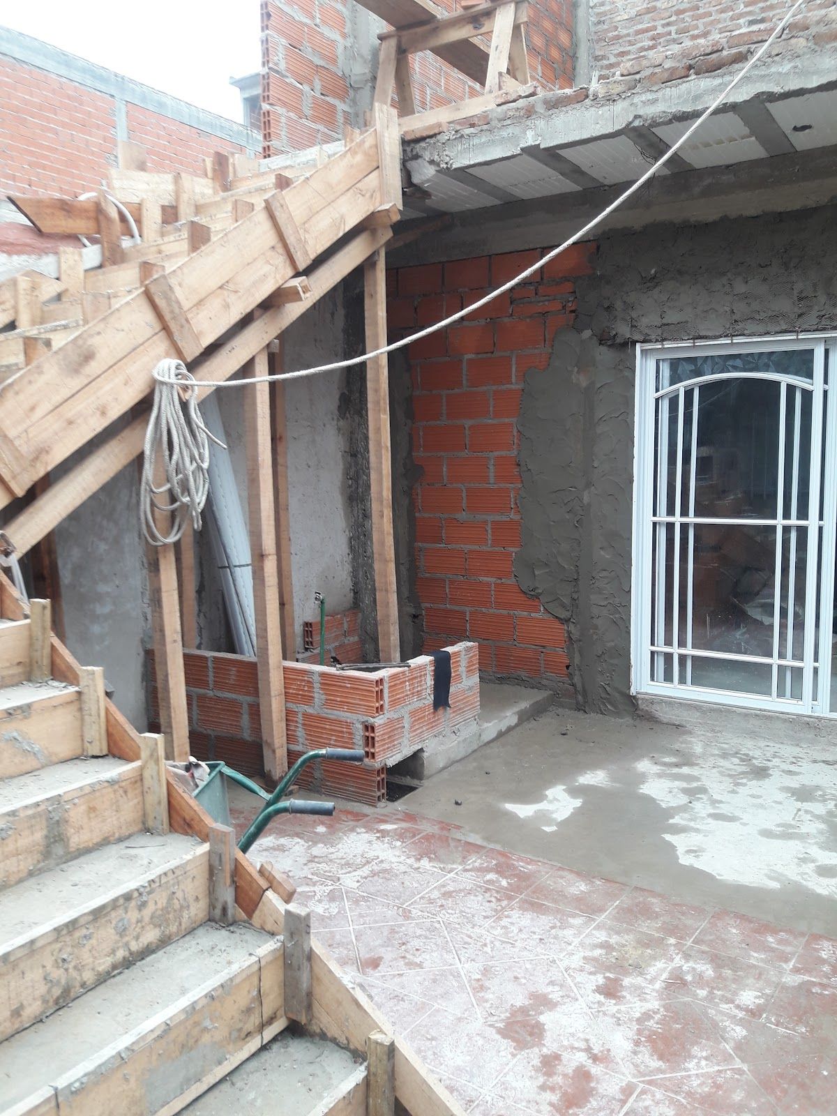 Dos personas reparando y lijando paredes blancas en una habitación luminosa y sin terminar durante una reforma.