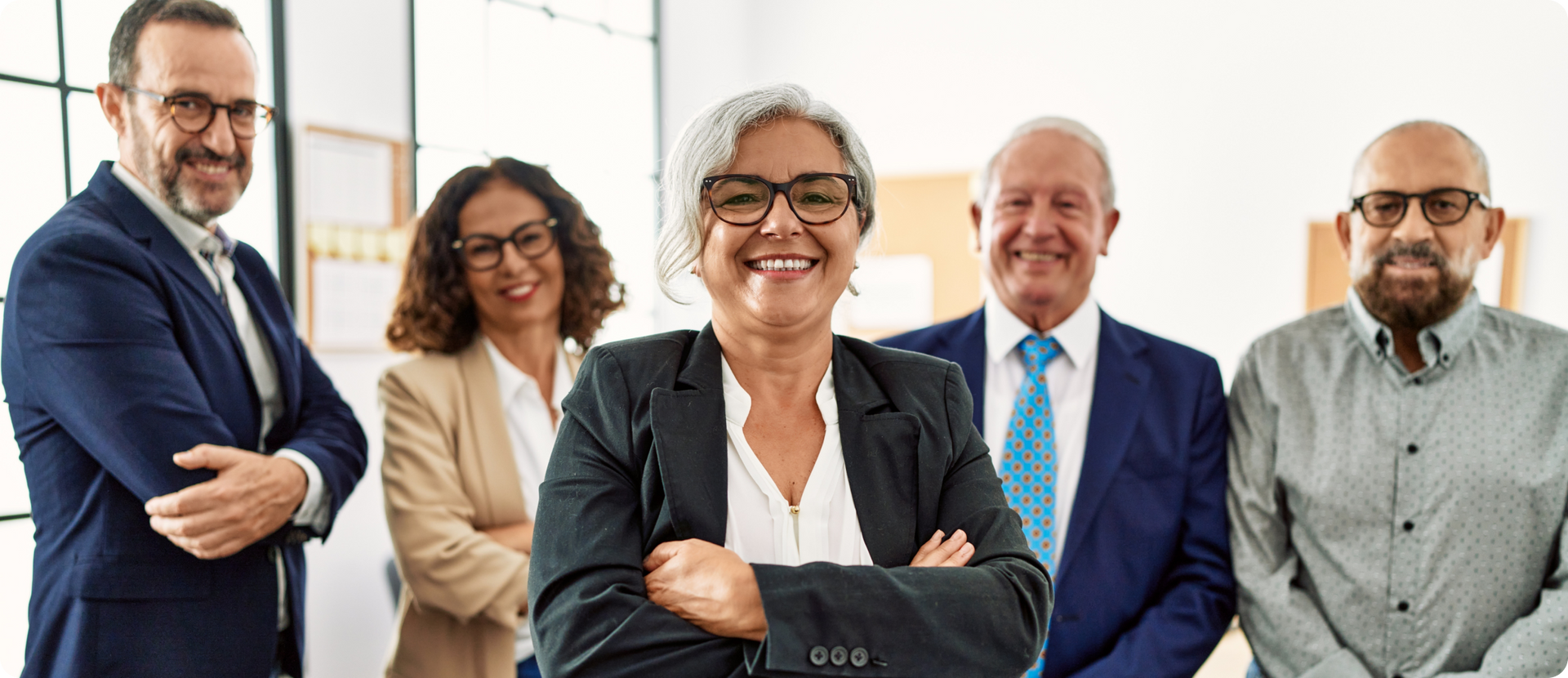 A group of five smiling business professionals pose for a photo in an office setting. They are diverse in age and race.