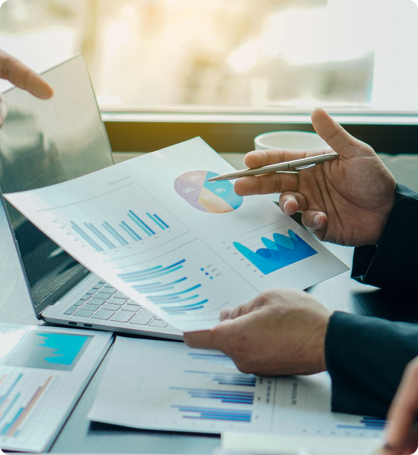Hands pointing to charts and a pie graph during a meeting near a laptop by a window.
