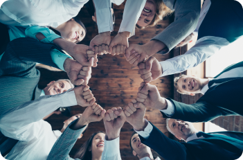 People in business attire fist-bumping in a circle, faces smiling, viewed from below.