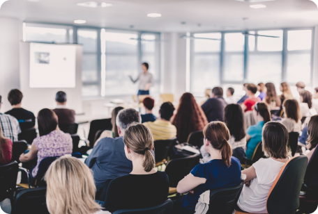 A classroom lecture with a presenter in front of a projector screen and an audience of seated people.