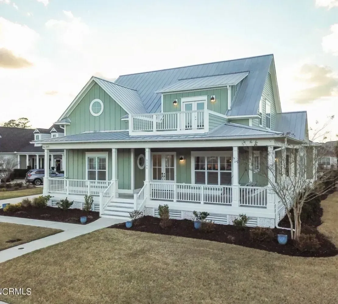 Blue two-story house with white trim, wraparound porch, and dormer windows on a grassy lawn