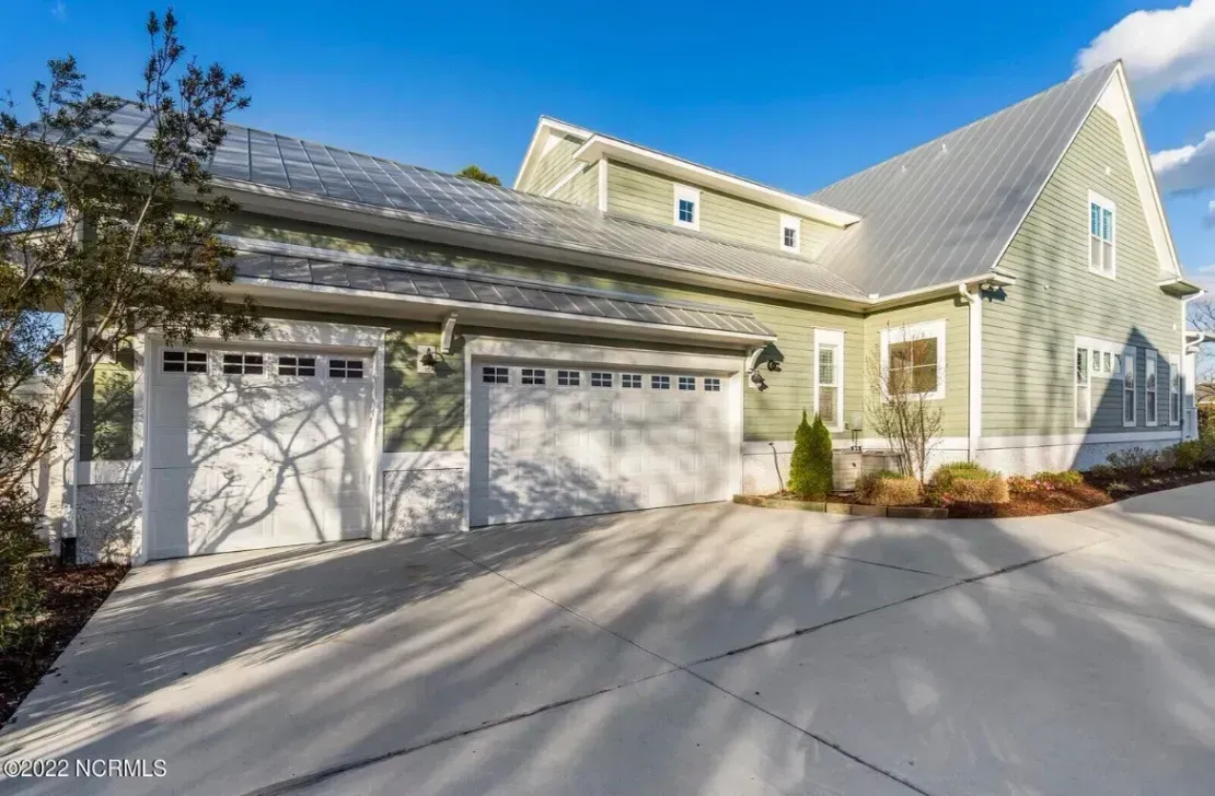 Large beige house with three white garage doors and a sloped driveway under a blue sky