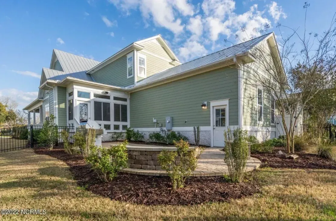 Light green house exterior with a screened porch, white trim, and a landscaped front yard under a blue sky