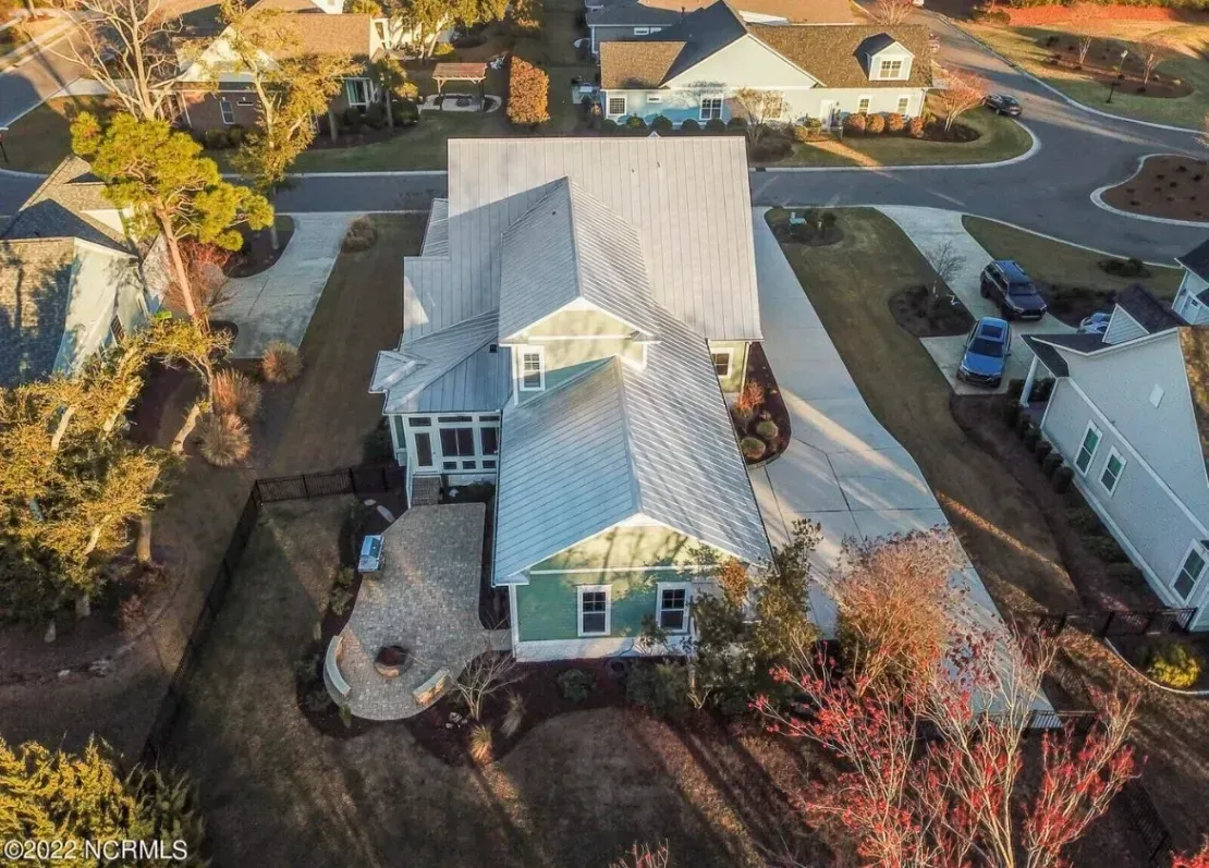 Aerial view of a white house with a gray roof, surrounded by trees and neighboring homes.