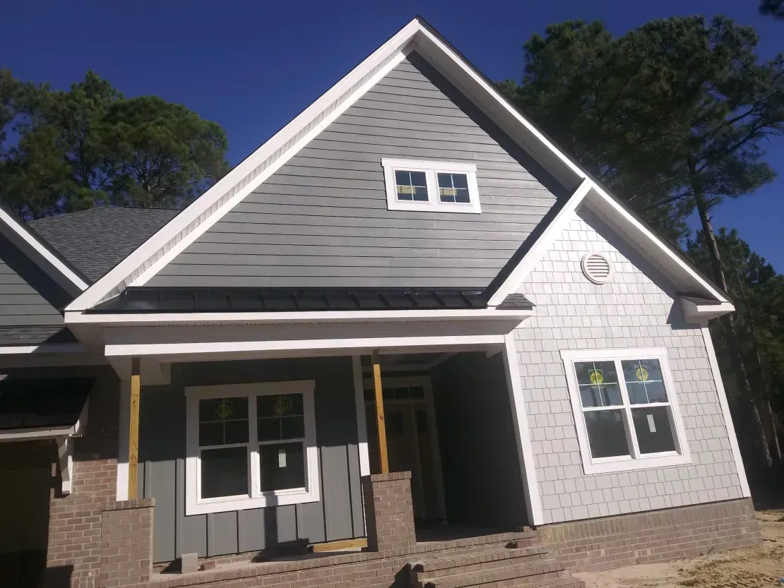White house exterior with gray roof, front porch, and new siding under construction