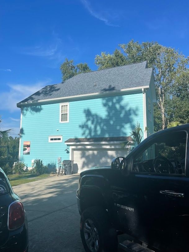 Light blue two-story house with white garage door, seen from a driveway under a clear blue sky