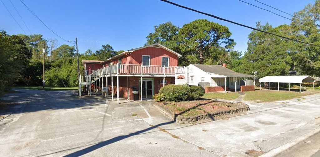 Red barn-style building with white columns and a large driveway on a sunny day