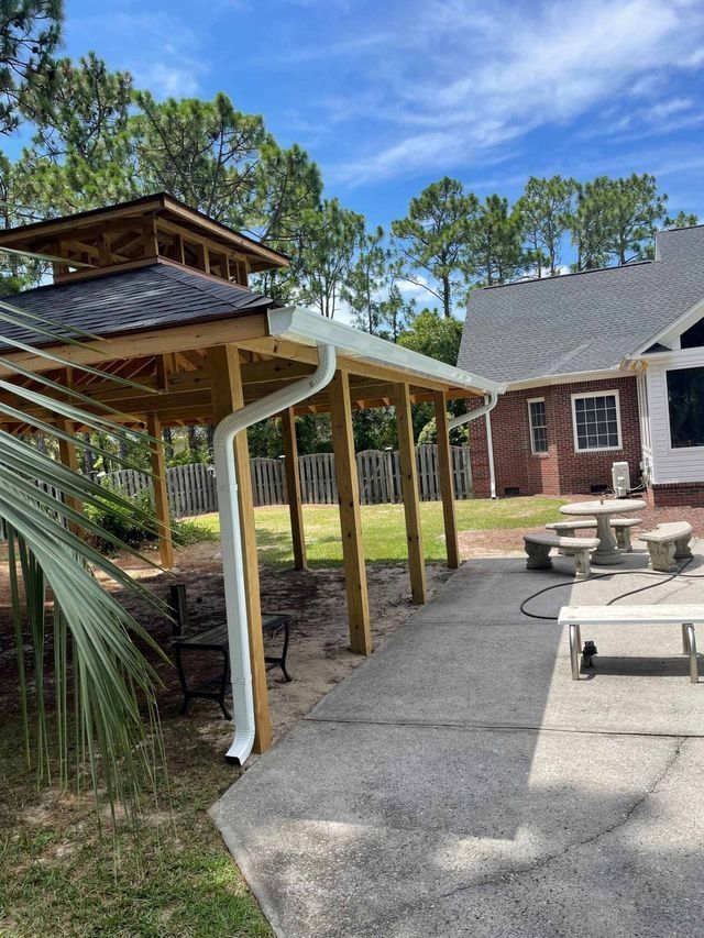 Backyard patio with ramp, pergola, brick house, and seating area under a blue sky