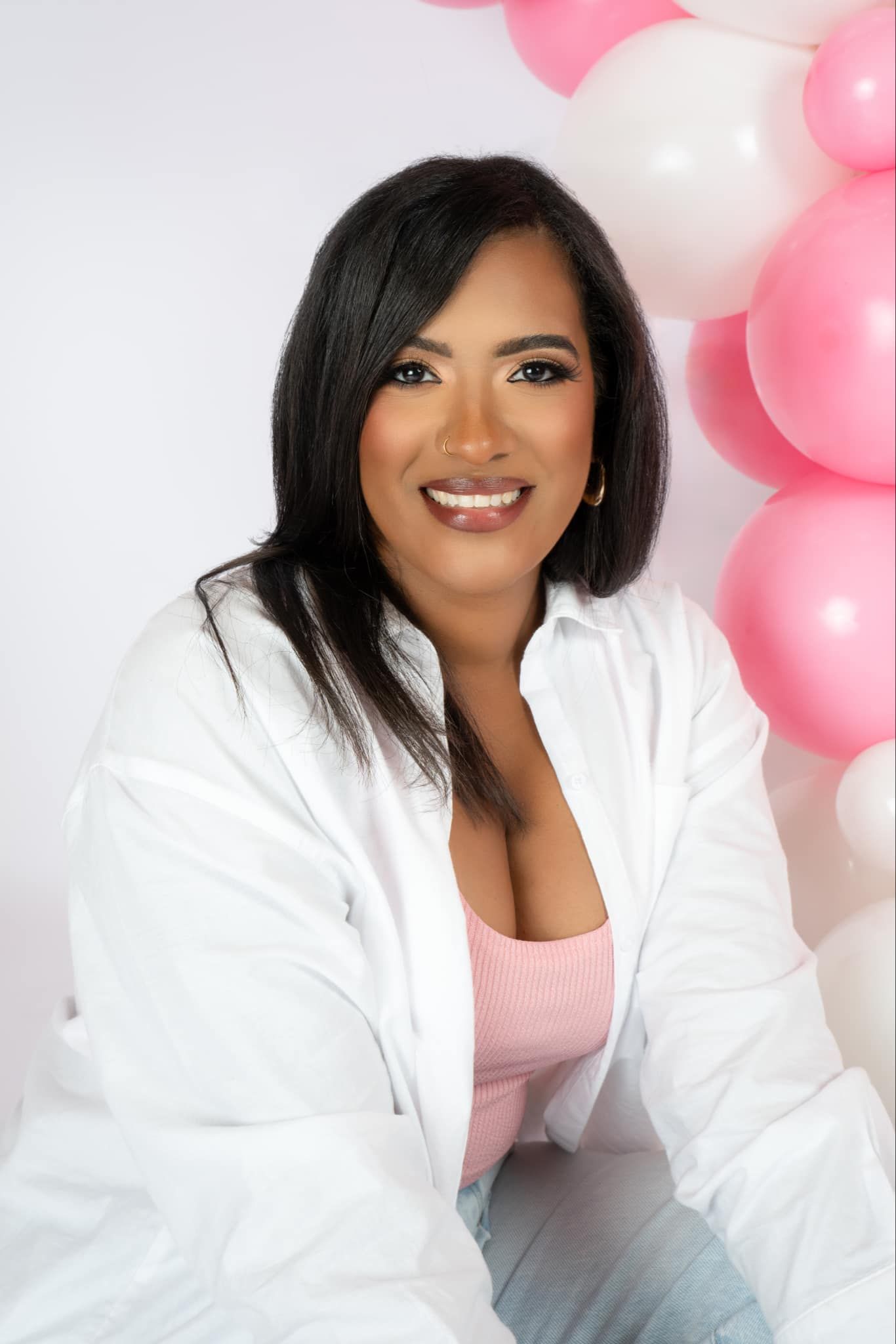 A woman is sitting in front of a bunch of pink and white balloons.