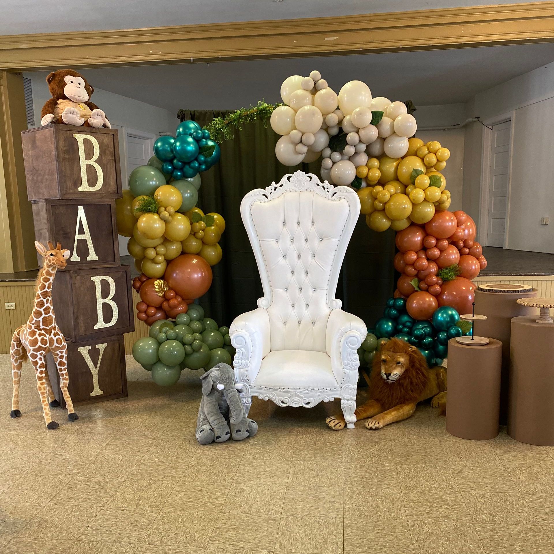 A white chair is surrounded by balloons and a giraffe and a lion.