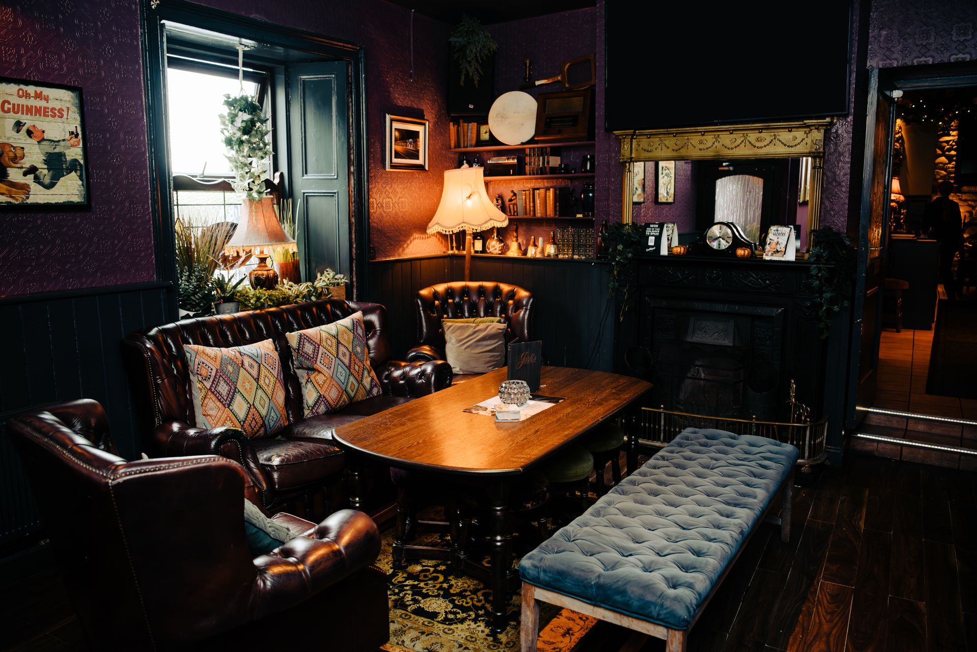 Cozy pub interior with leather seating, wooden table, fireplace, and dim lighting.