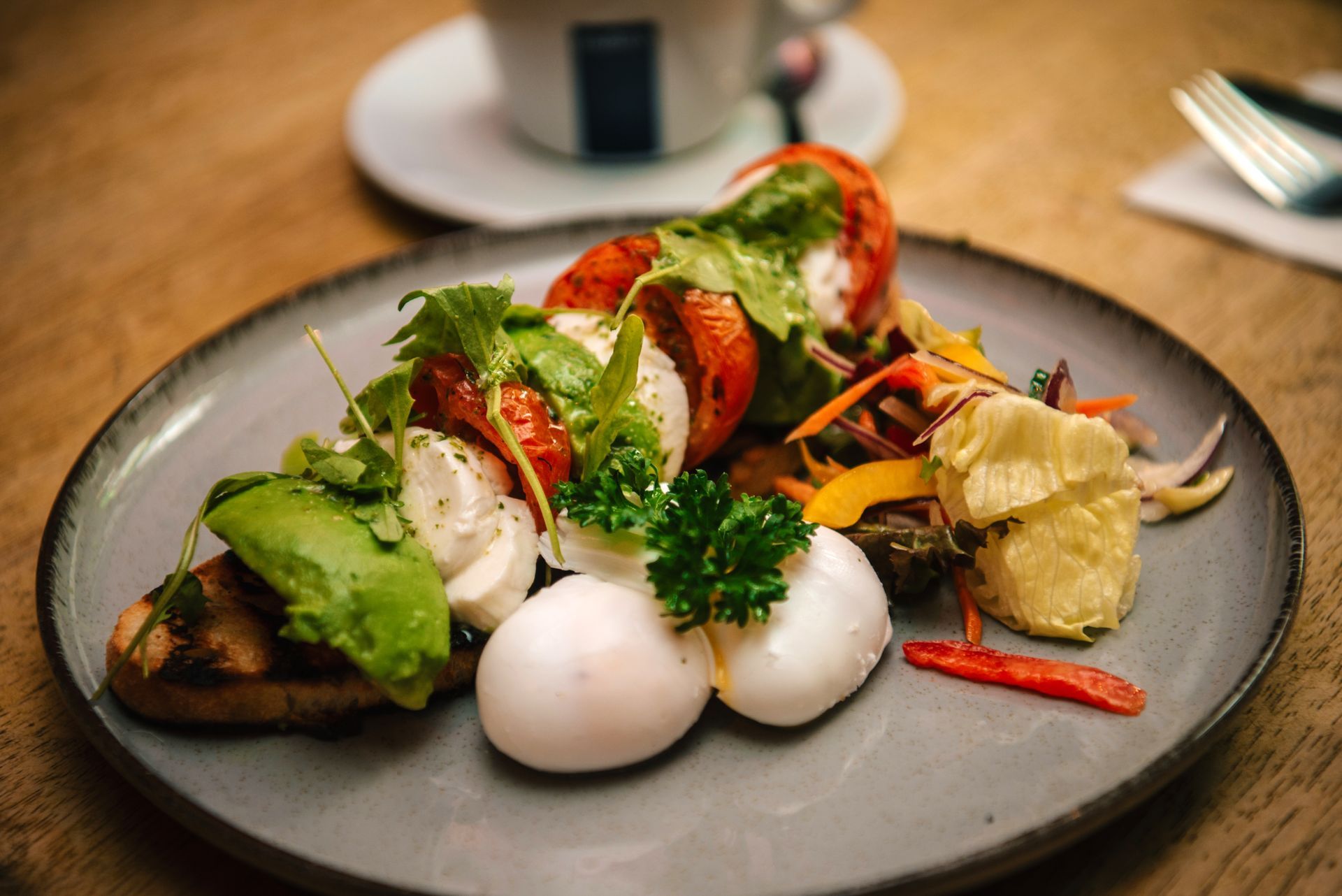 Plate with roasted tomatoes, avocado toast, poached eggs, vegetables, and a cup of coffee.