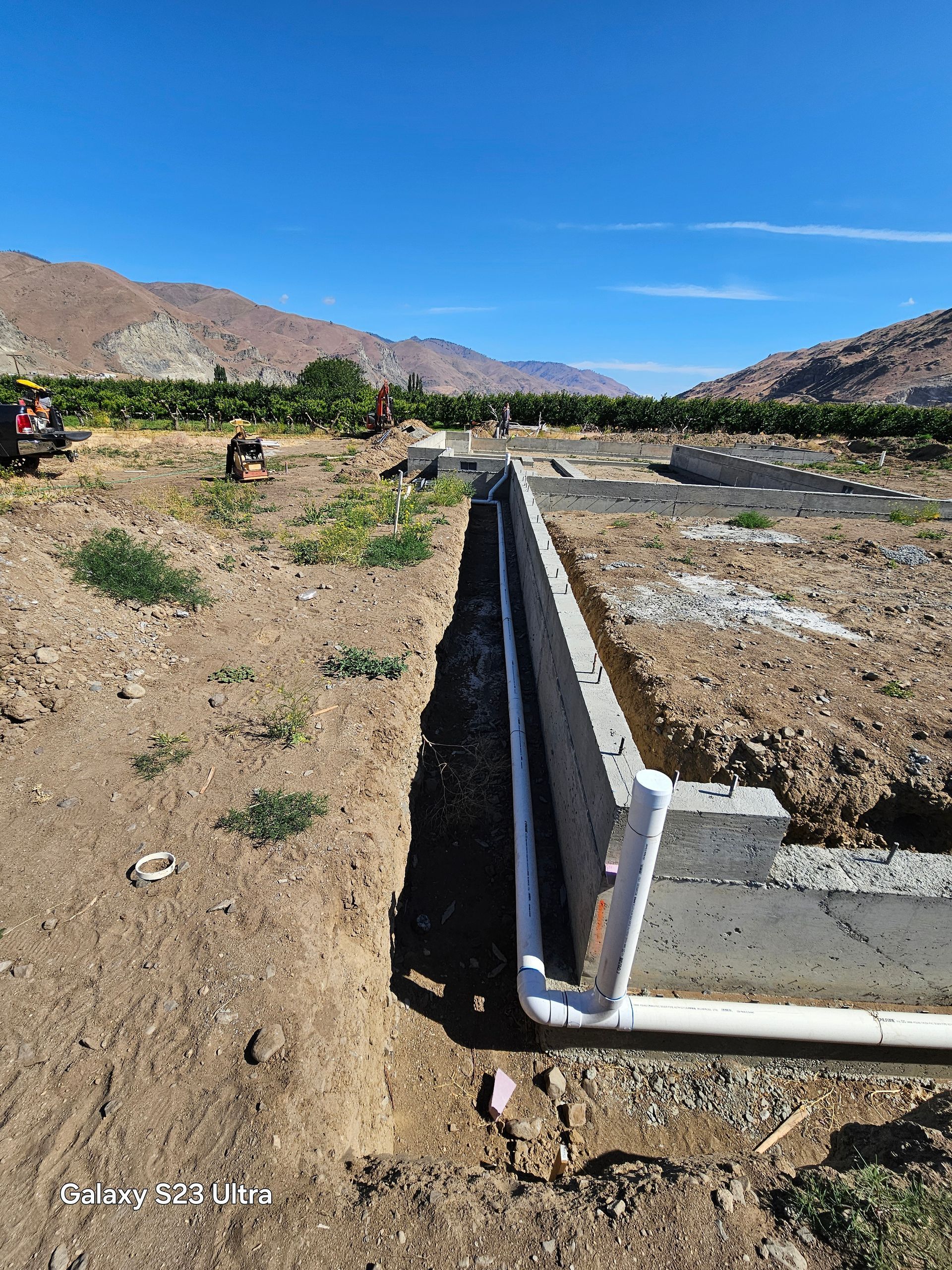 Construction site with trench and white pipe in arid landscape with mountains.