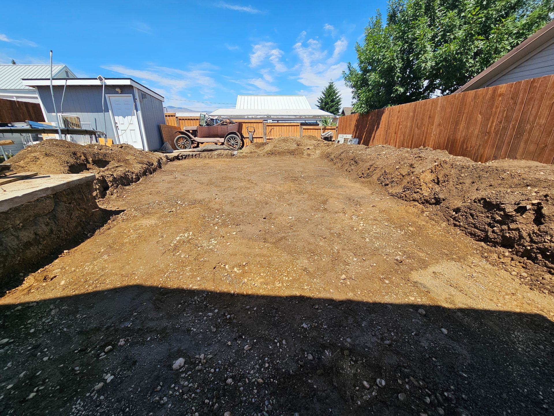 Backyard dirt excavation for a construction project, with dirt piles and fencing visible.
