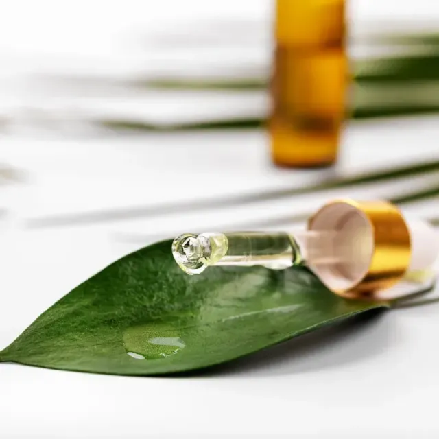 A dropper of oil is sitting on a green leaf.