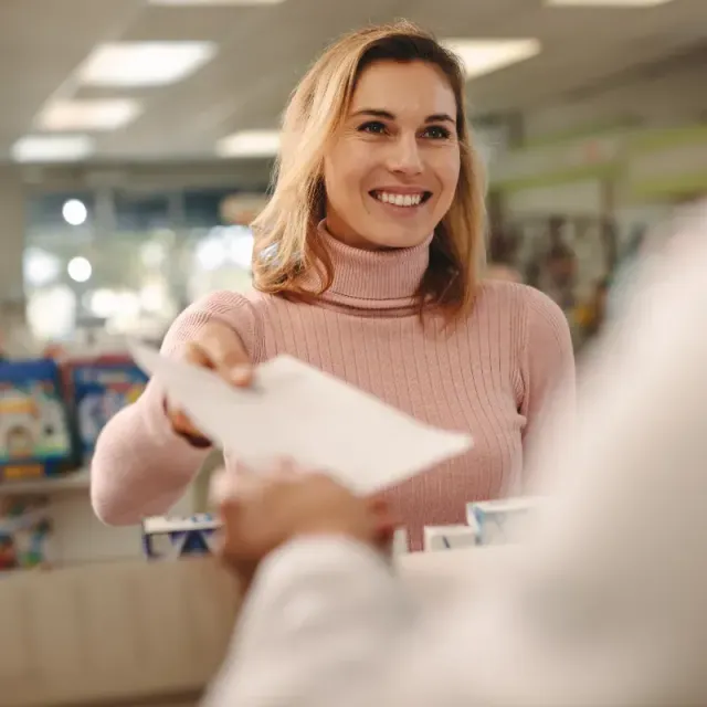 A woman is giving a prescription to a pharmacist in a pharmacy.