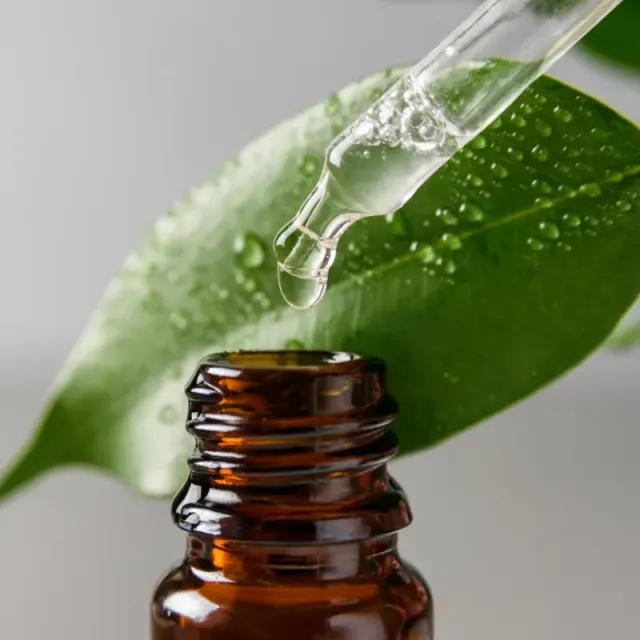 A liquid is being poured from a pipette into a bottle. There is a leaf in the background.