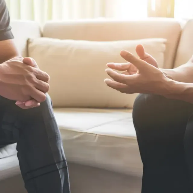 Two people are sitting on a couch talking to each other.