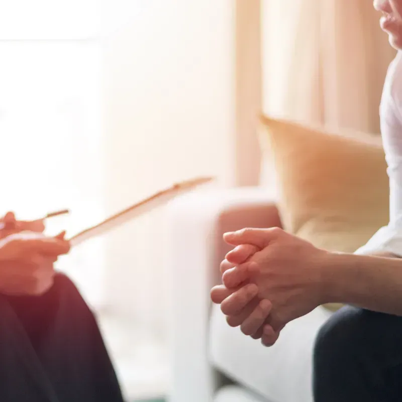 A woman is sitting on a couch talking to a doctor.