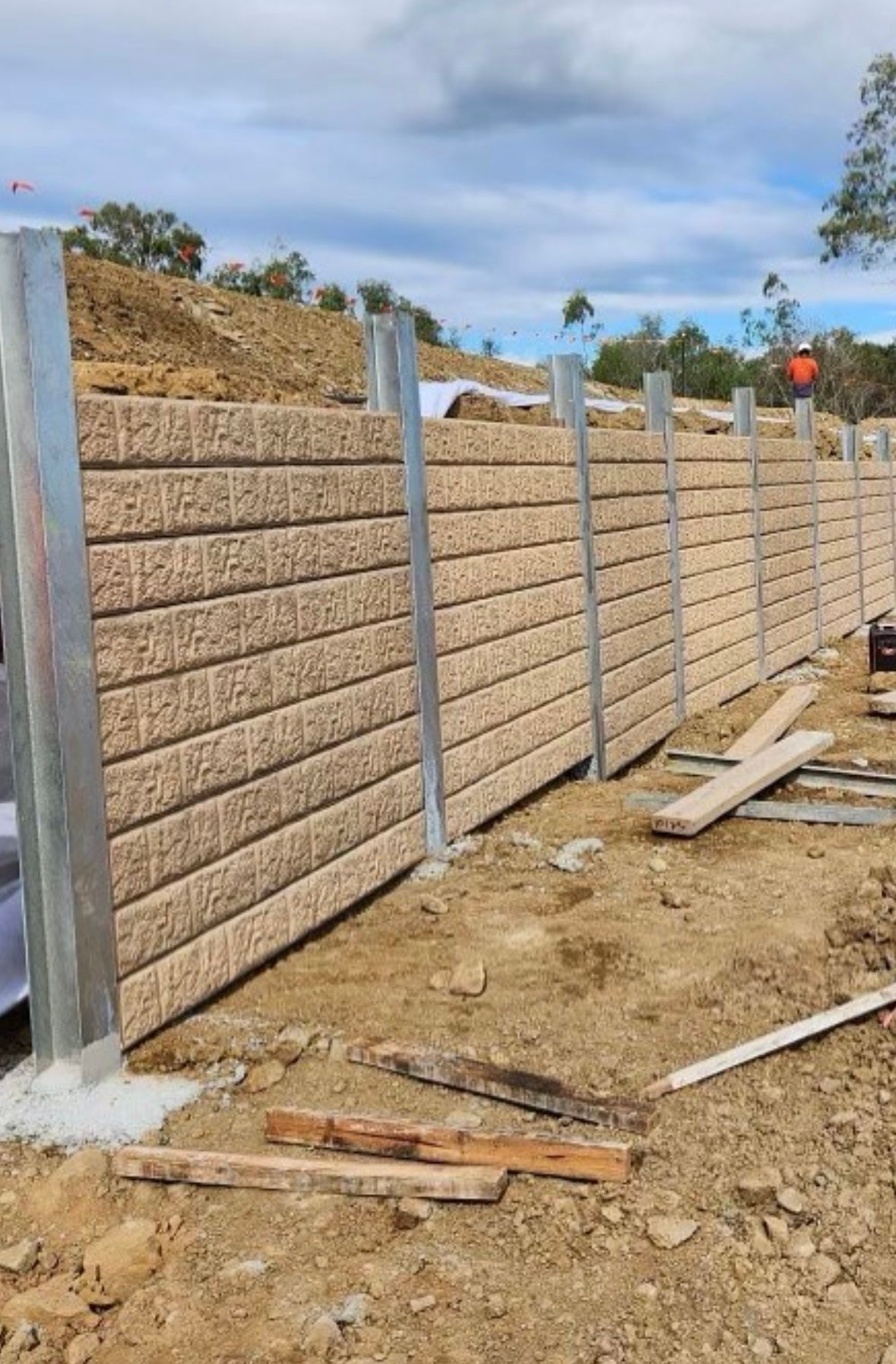 A sleeper concrete retaining wall is being built on top of a dirt field.