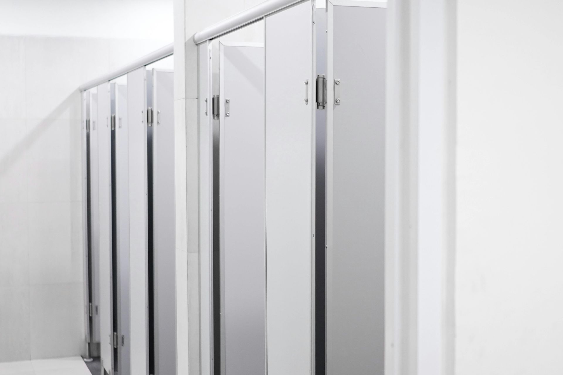 Row of office stalls that are metallic looking which have been cleaned spotlessly by janitors