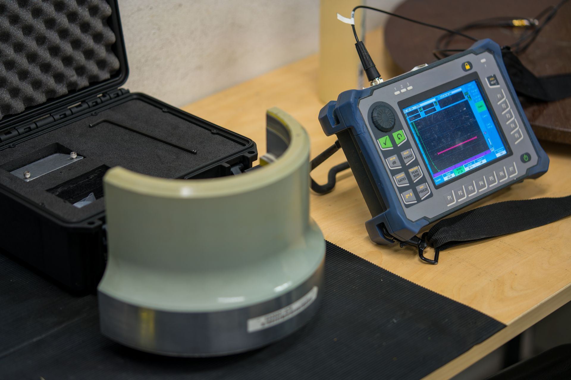 Portable industrial testing device with display screen and sensor attachment on a workbench.