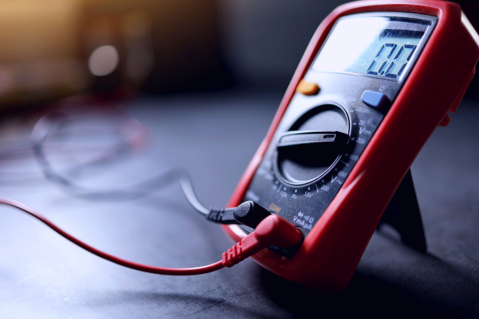 Red digital multimeter with test leads connected, displaying a reading on its LCD screen