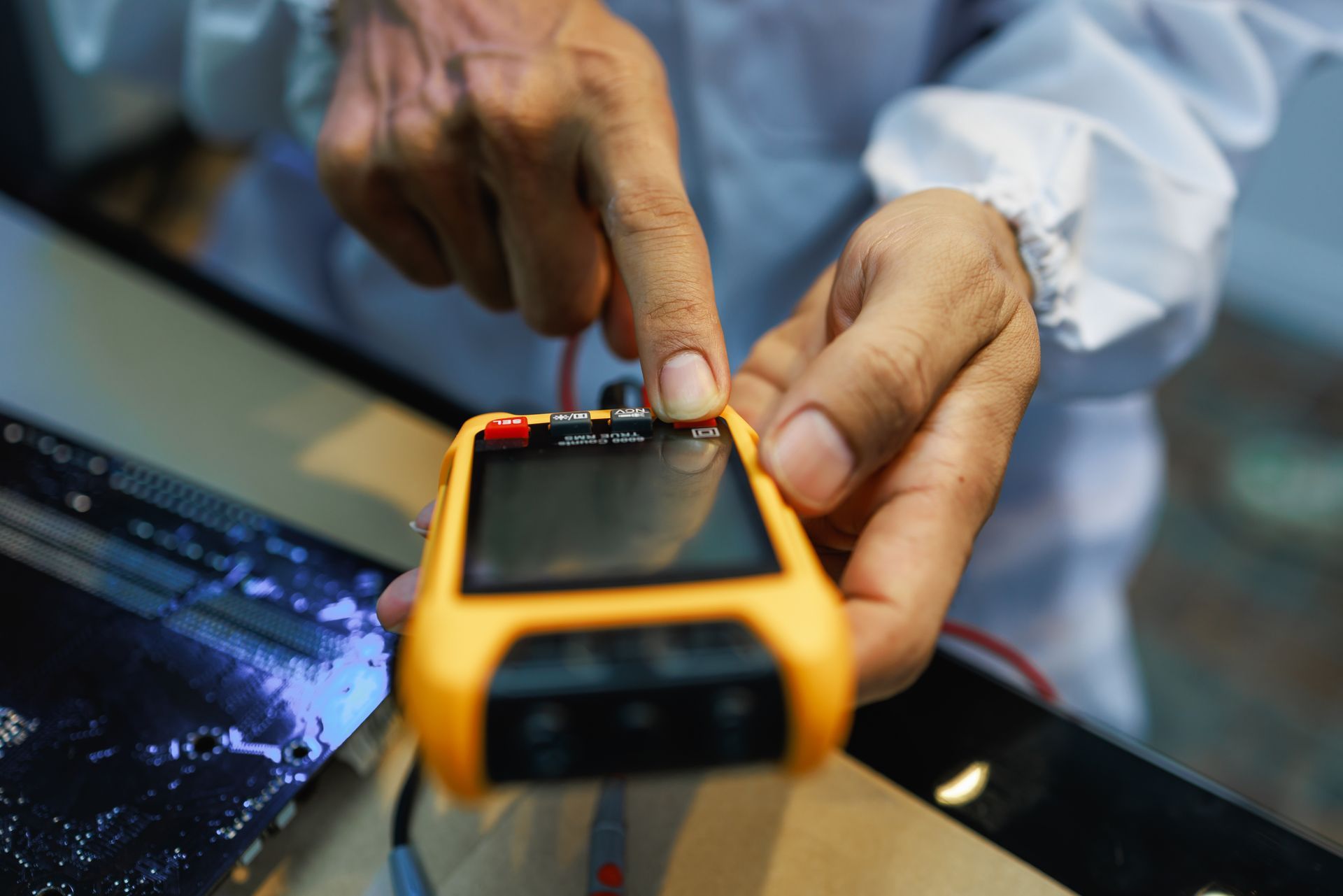 Technician turns the switch of the precision multi calibrator for calibration multimeter. hands checking a yellow handheld electronic meter beside a laptop.