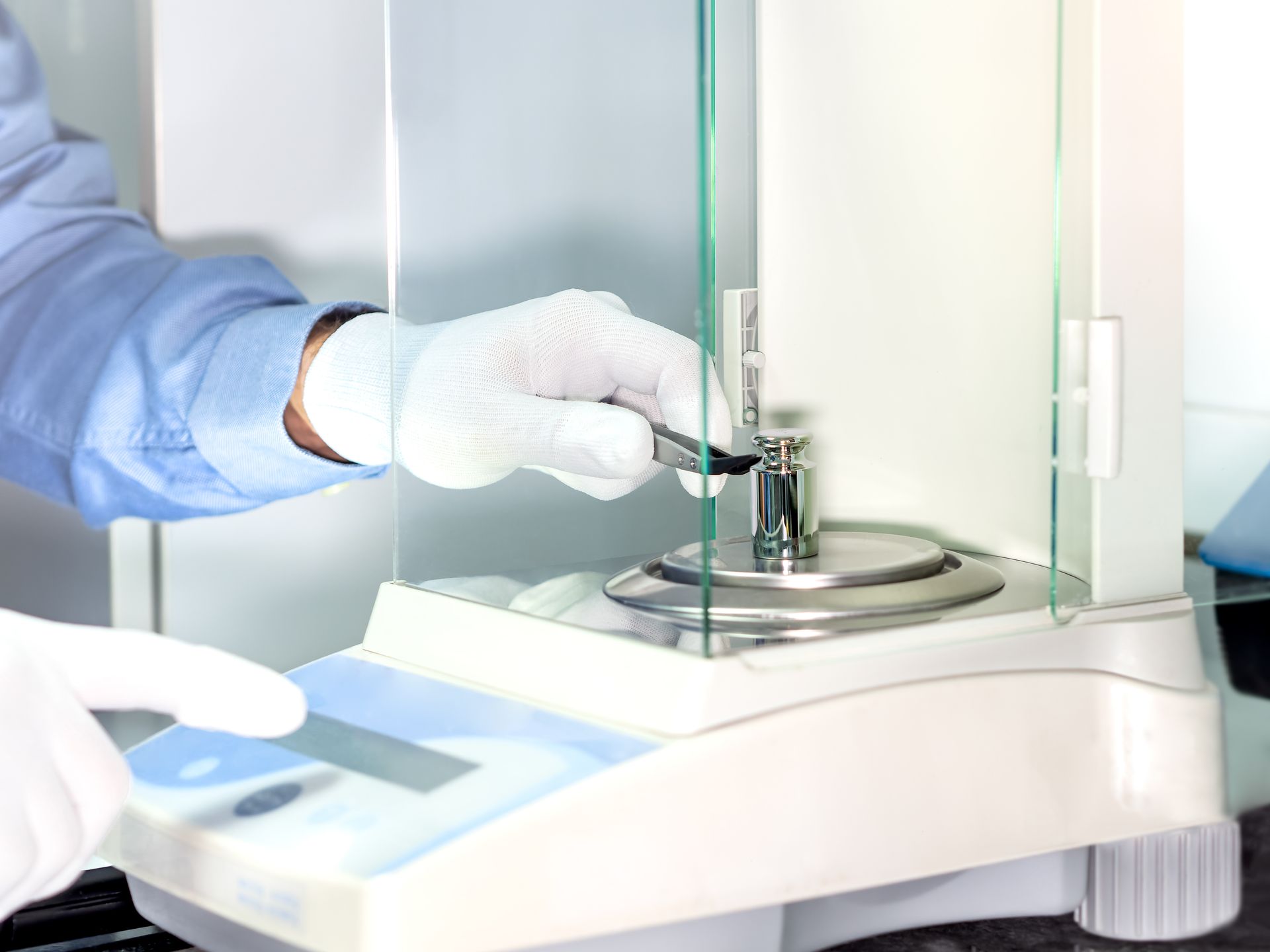 Steel weight being positioned by operator, representing on-site calibration on lab analytical scale.
