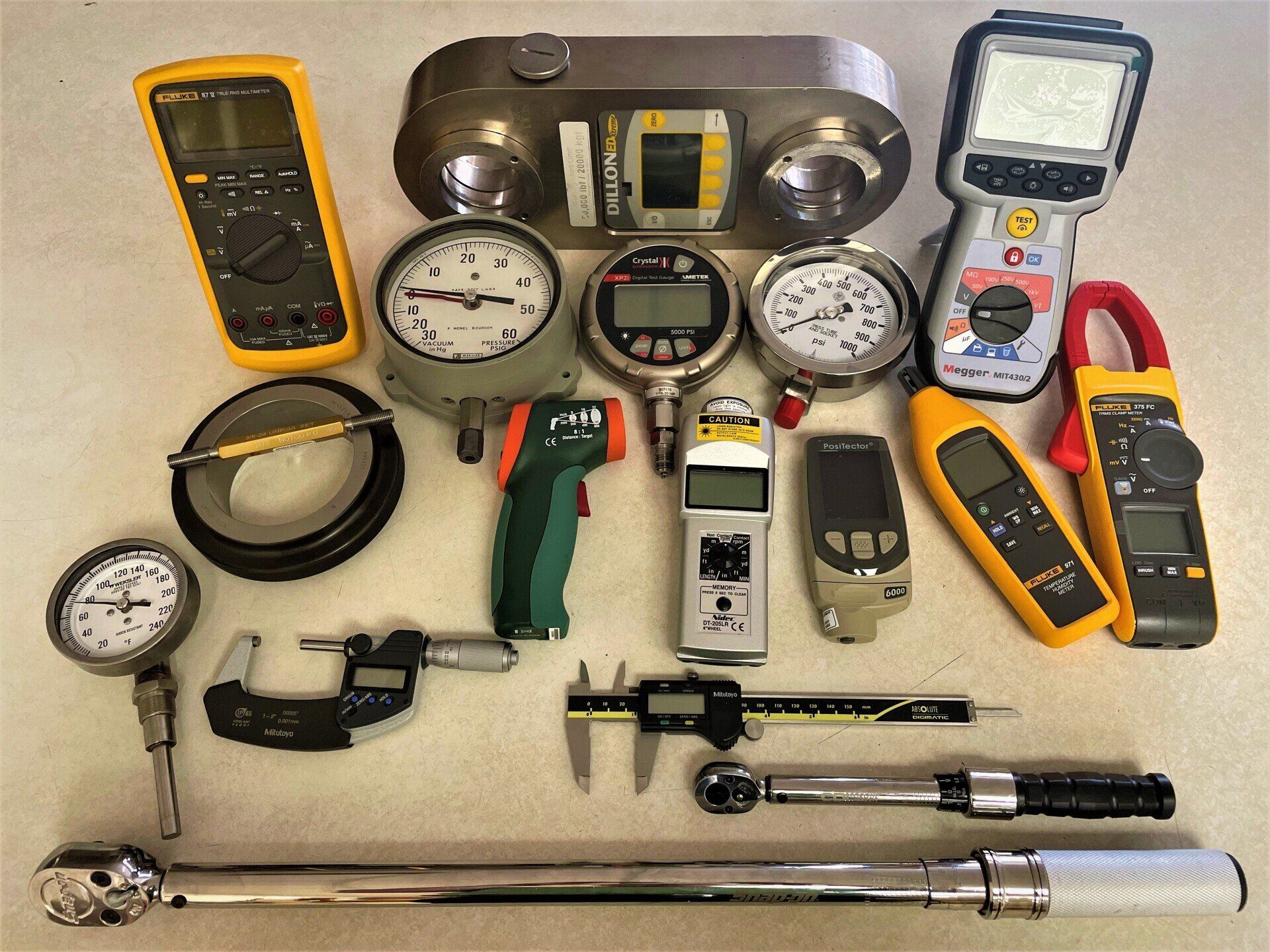 Assorted measuring tools and meters arranged on a tabletop, including gauges, multimeters, and calipers.