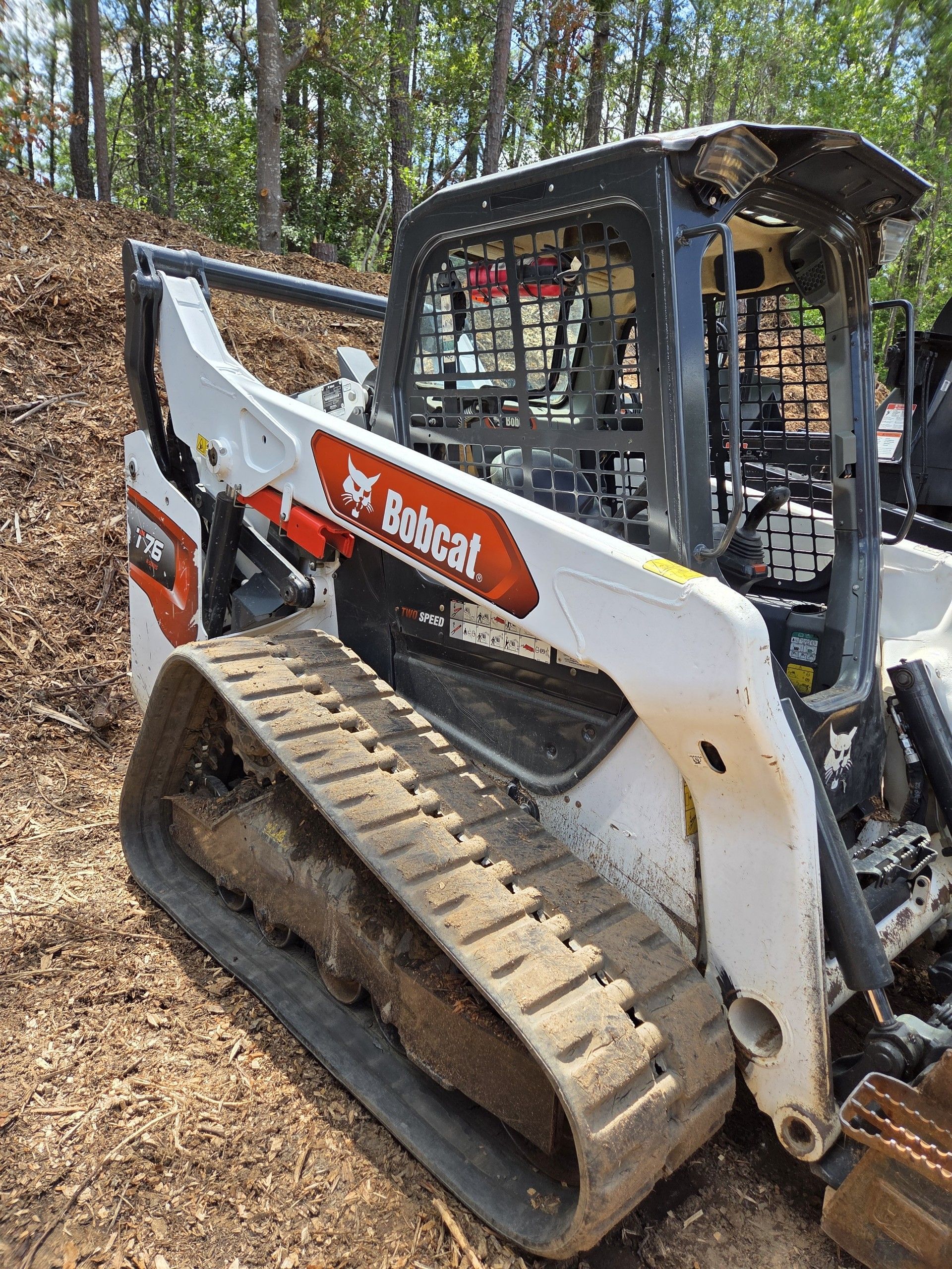 Bobcat skid steer with tracks parked on a wooded dirt path in fall leaves Bobcat skid steer with tracks parked on a wooded dirt path in fall leaves