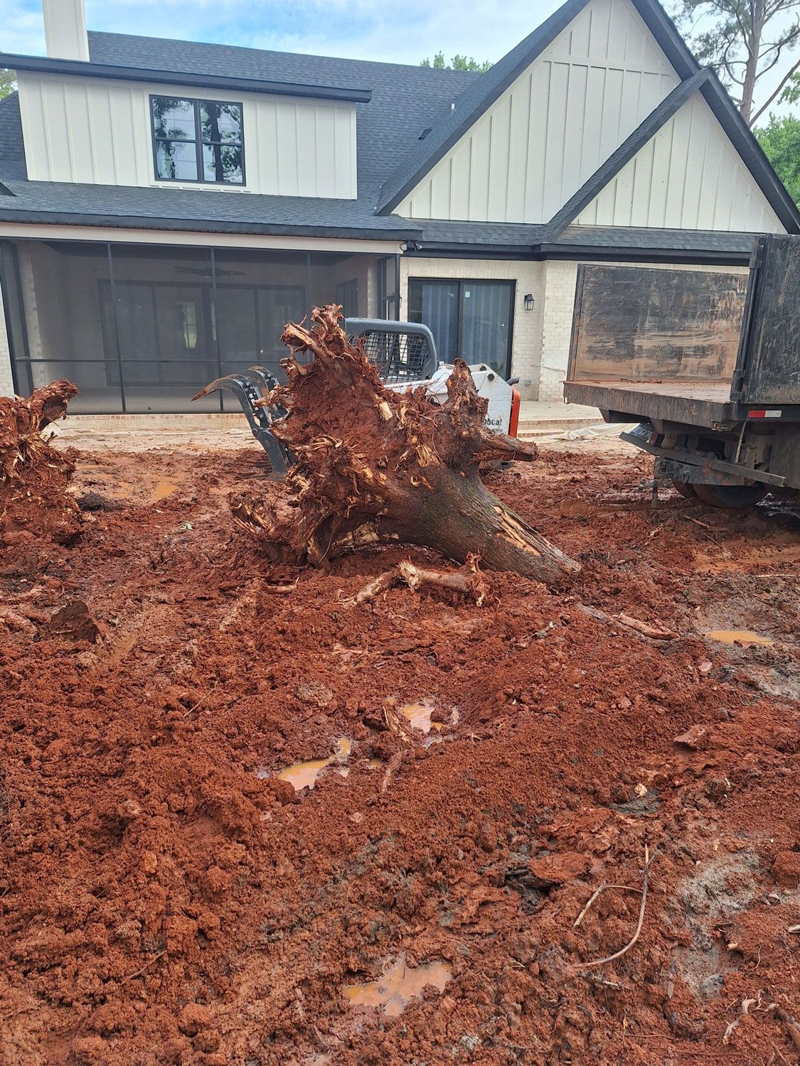 Uprooted tree stump and muddy debris in front of a house with a truck parked beside it Uprooted tree stump and muddy debris in front of a house with a truck parked beside it