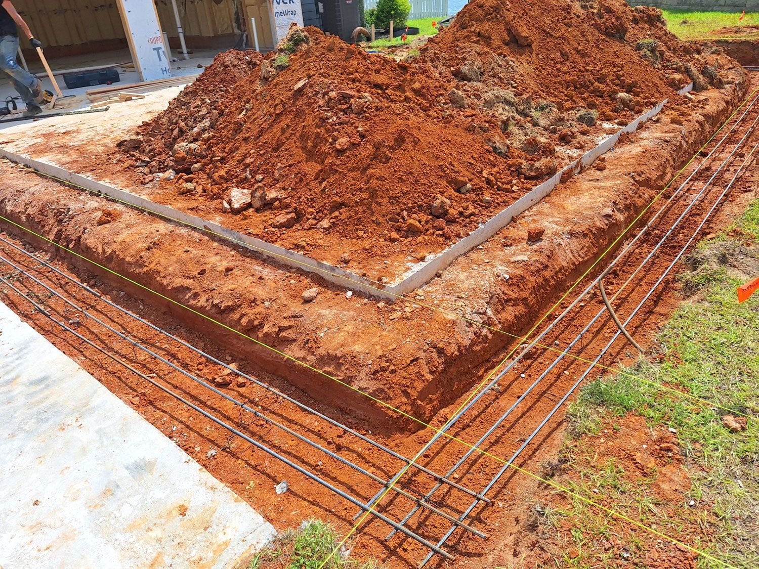 Construction site with a deep foundation trench, exposed rebar, and a pile of reddish soil. Construction site with a deep foundation trench, exposed rebar, and a pile of reddish soil.