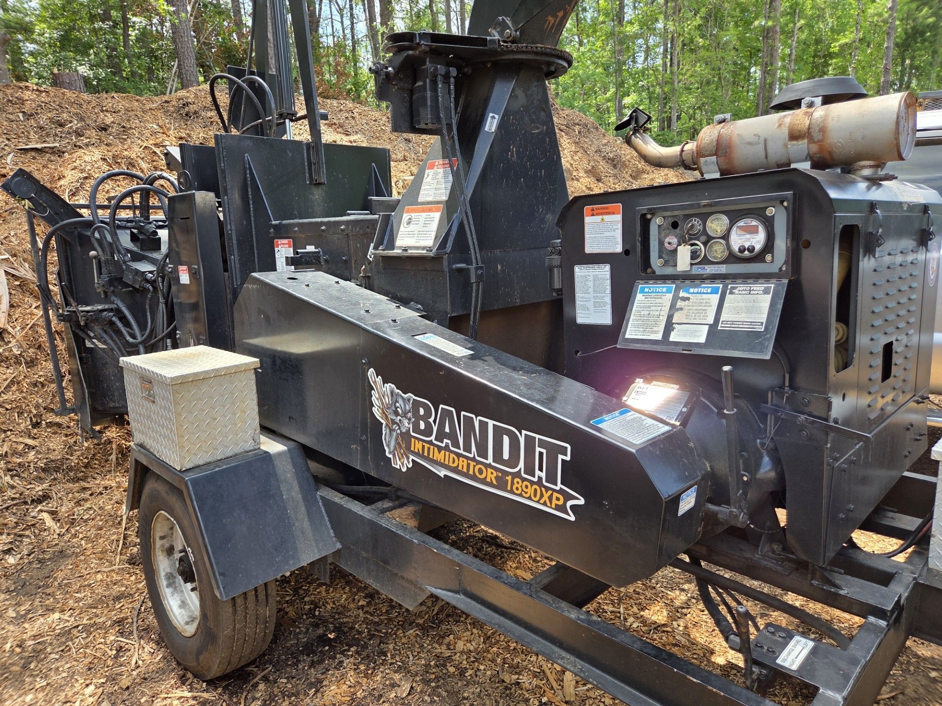 Black Bandit wood chipper trailer with control panel parked outdoors in a wooded area Black Bandit wood chipper trailer with control panel parked outdoors in a wooded area