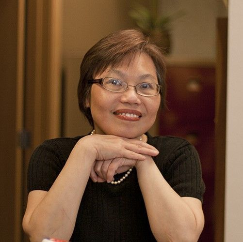 Smiling person with glasses resting chin on hands in a black top