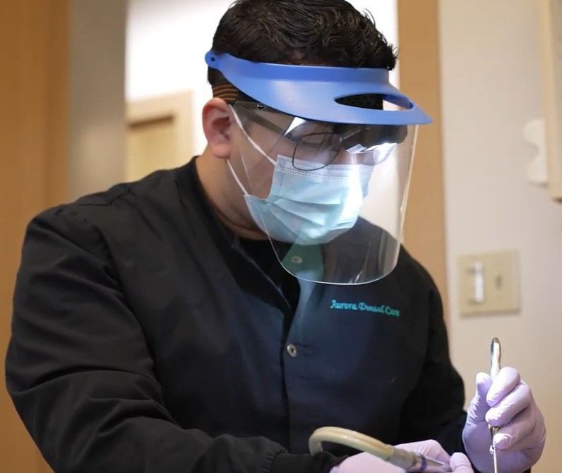 Dentist in face shield and mask working with dental tools in a clinic room